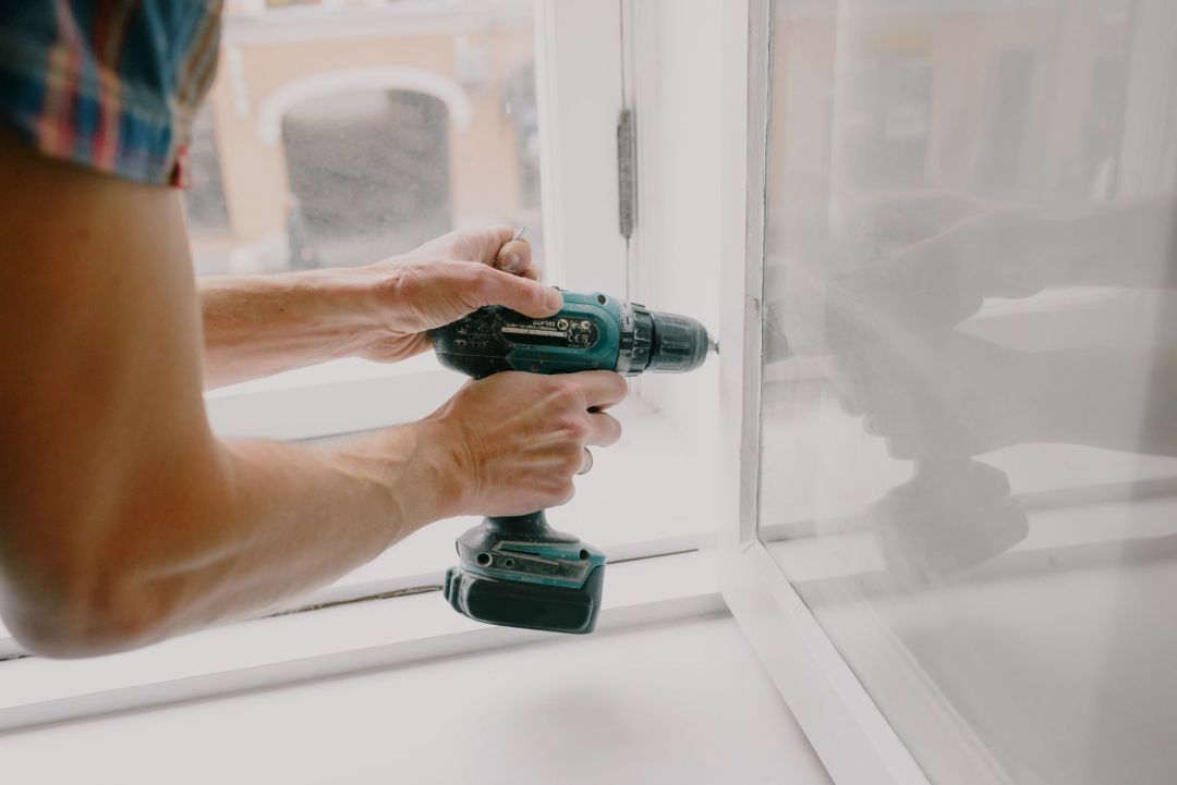 Monteur verschraubt einen Fensterrahmen in der Laibung eines Neubaus