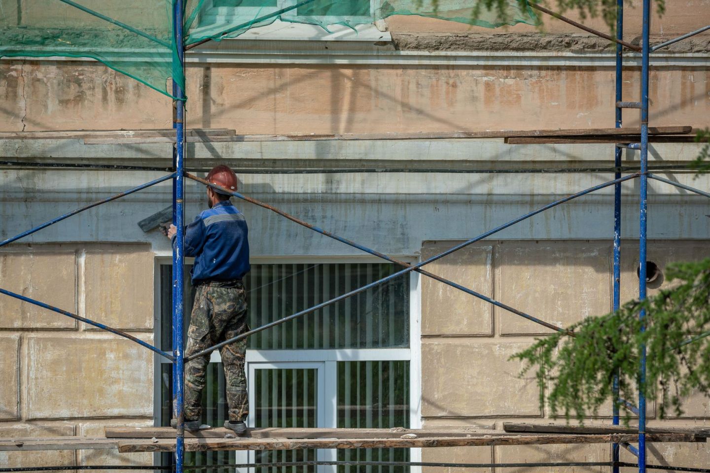 Handwerker auf einem Gerüst vor der Fassade eines Wohnhauses während der Sanierung